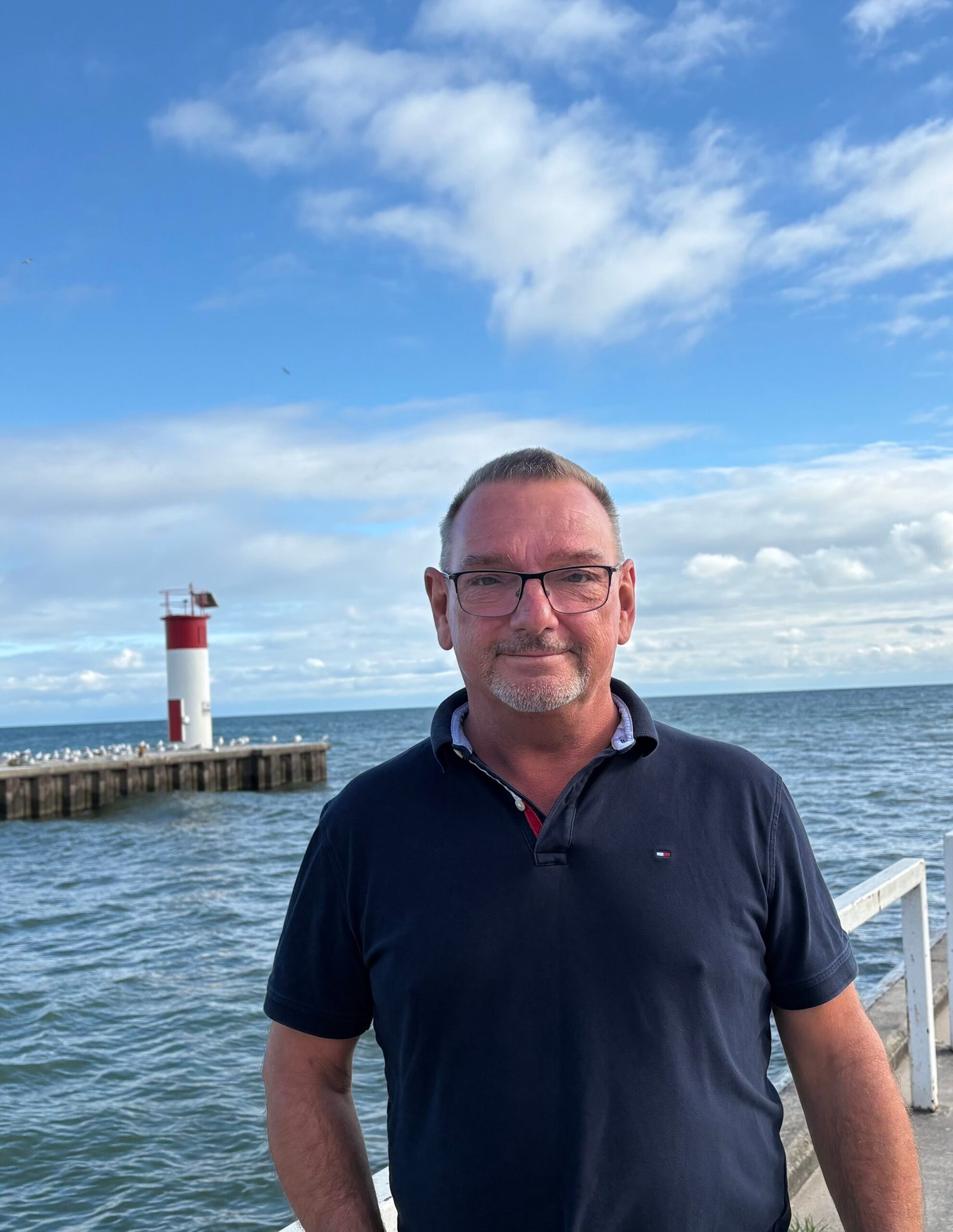 Portrait of Bill Jukes on the pier with the red and white harbour light behind him